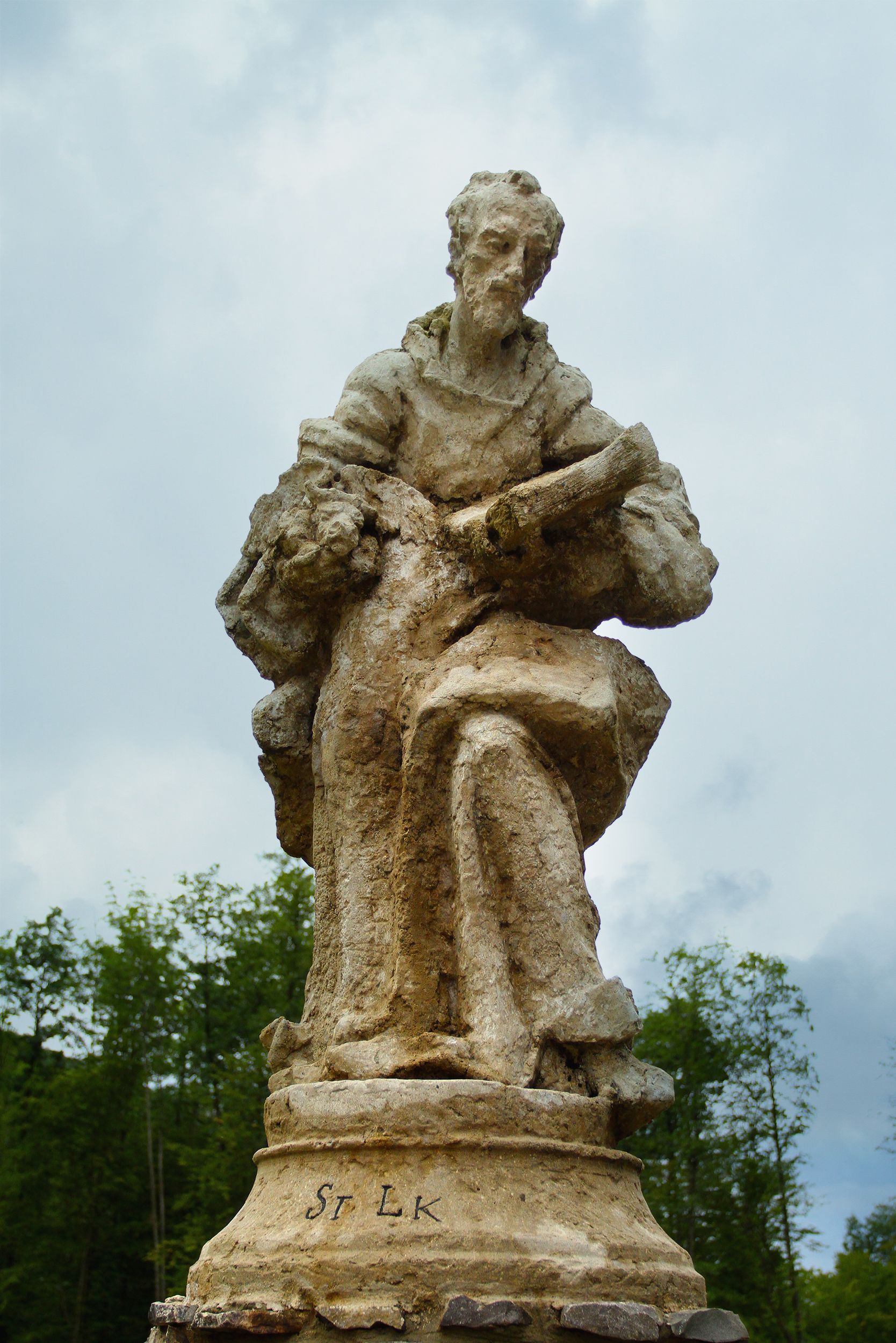 Weathered stone statue depicting a seated figure against a cloudy sky.