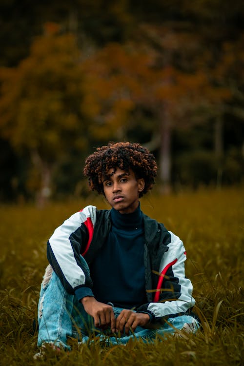 African American teenager in trendy outfit sitting on grass field