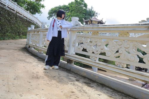 Free Woman in stylish attire stands on a decorative bridge, enjoying a sunny day outdoors. Stock Photo