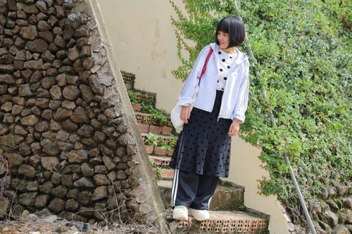 Free Stylish woman with short hair in polka dot attire standing on stone steps surrounded by greenery. Stock Photo