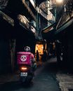 Faceless delivery man riding motorcycle on city street at night