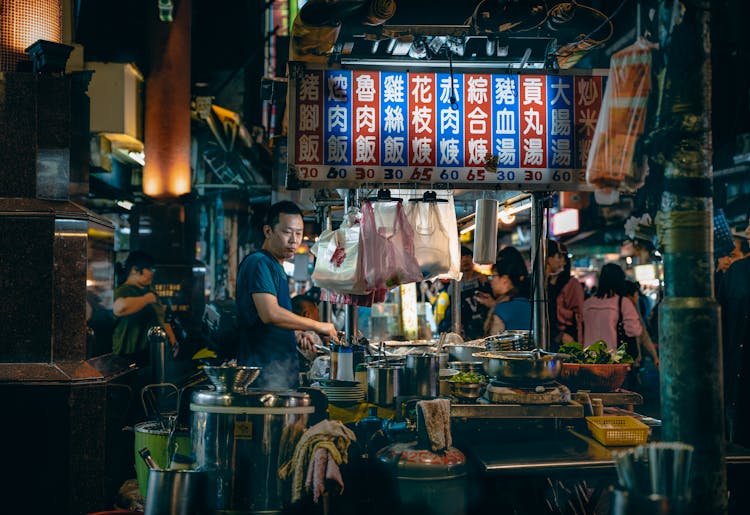 Asian Chef Cooking Food Under Bright Signboard With Hieroglyphs