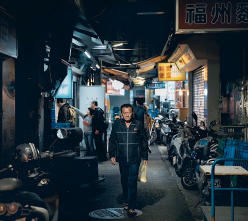 夜に建物の間の歩道を歩く成熟したアジア人男性