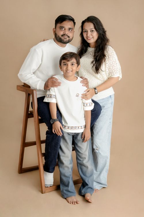 Free A family of three posing joyfully against a neutral beige backdrop in casual attire. Stock Photo