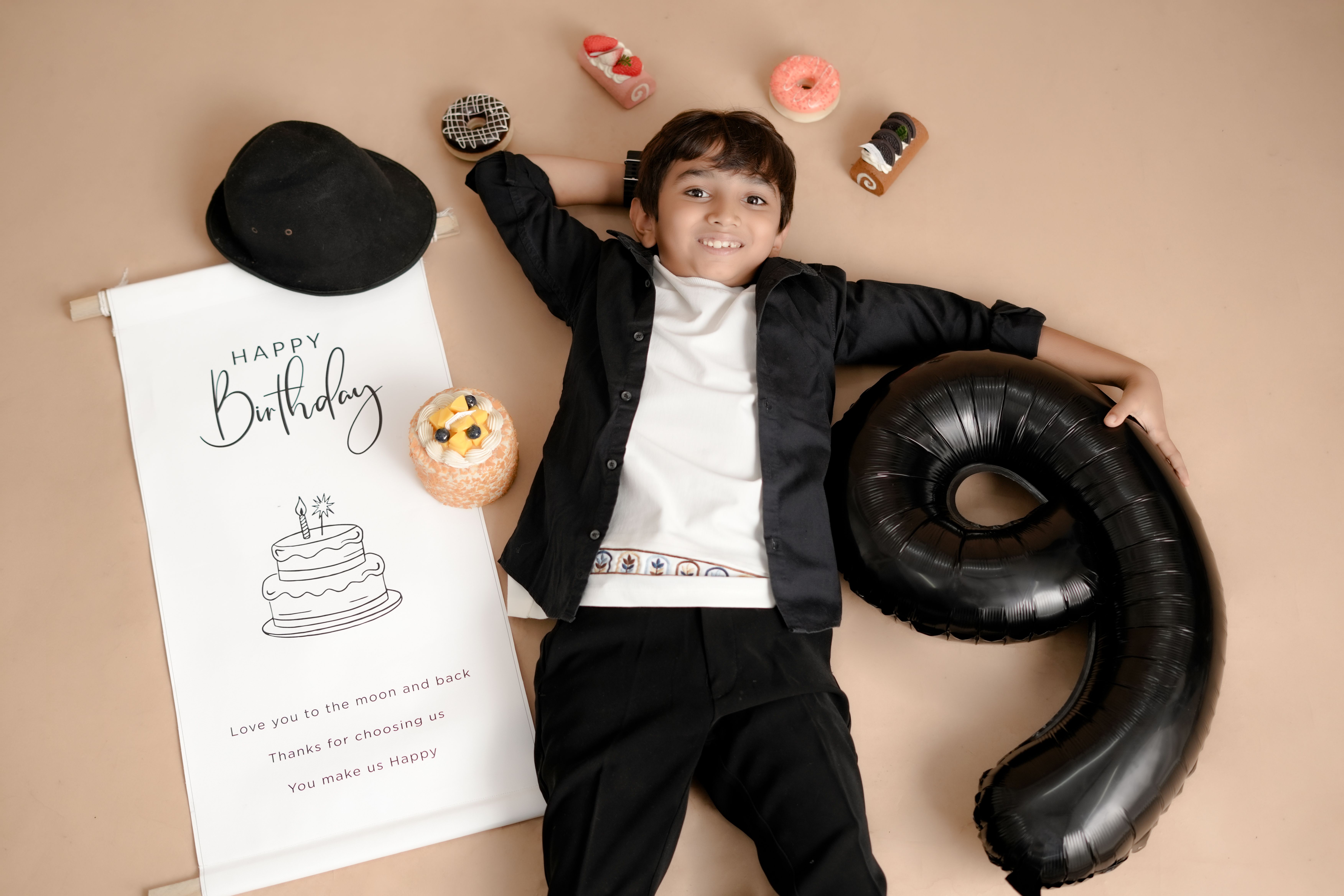 Young boy celebrating his 9th birthday with balloons and treats, lying happily.
