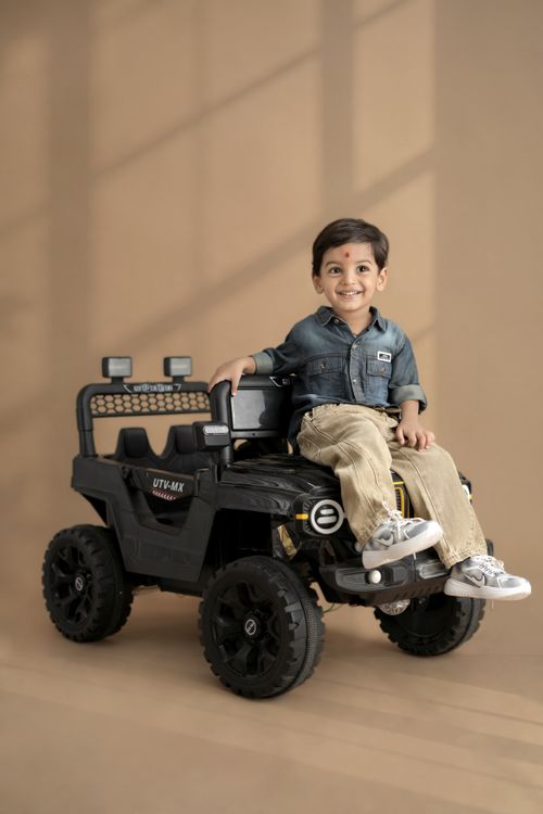 Free A cheerful child sits in a toy car in a bright indoor setting, exuding joy and playfulness. Stock Photo