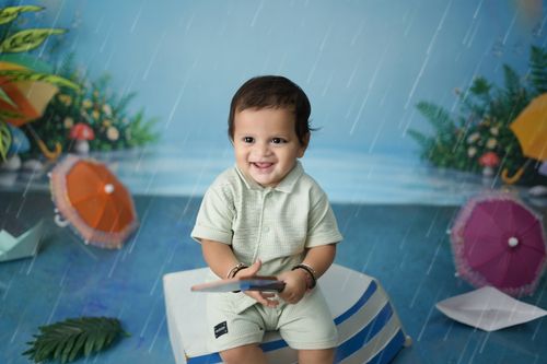 Free Cute baby smiling amidst colorful umbrellas in rainy indoor setting. Stock Photo