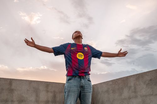 Free A man in a team jersey stands with arms open under a twilight sky, feeling liberated. Stock Photo
