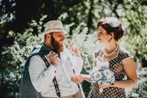 Free Vintage styled couple smiling in a sunny outdoor setting, dressed in retro attire, capturing a joyful moment. Stock Photo
