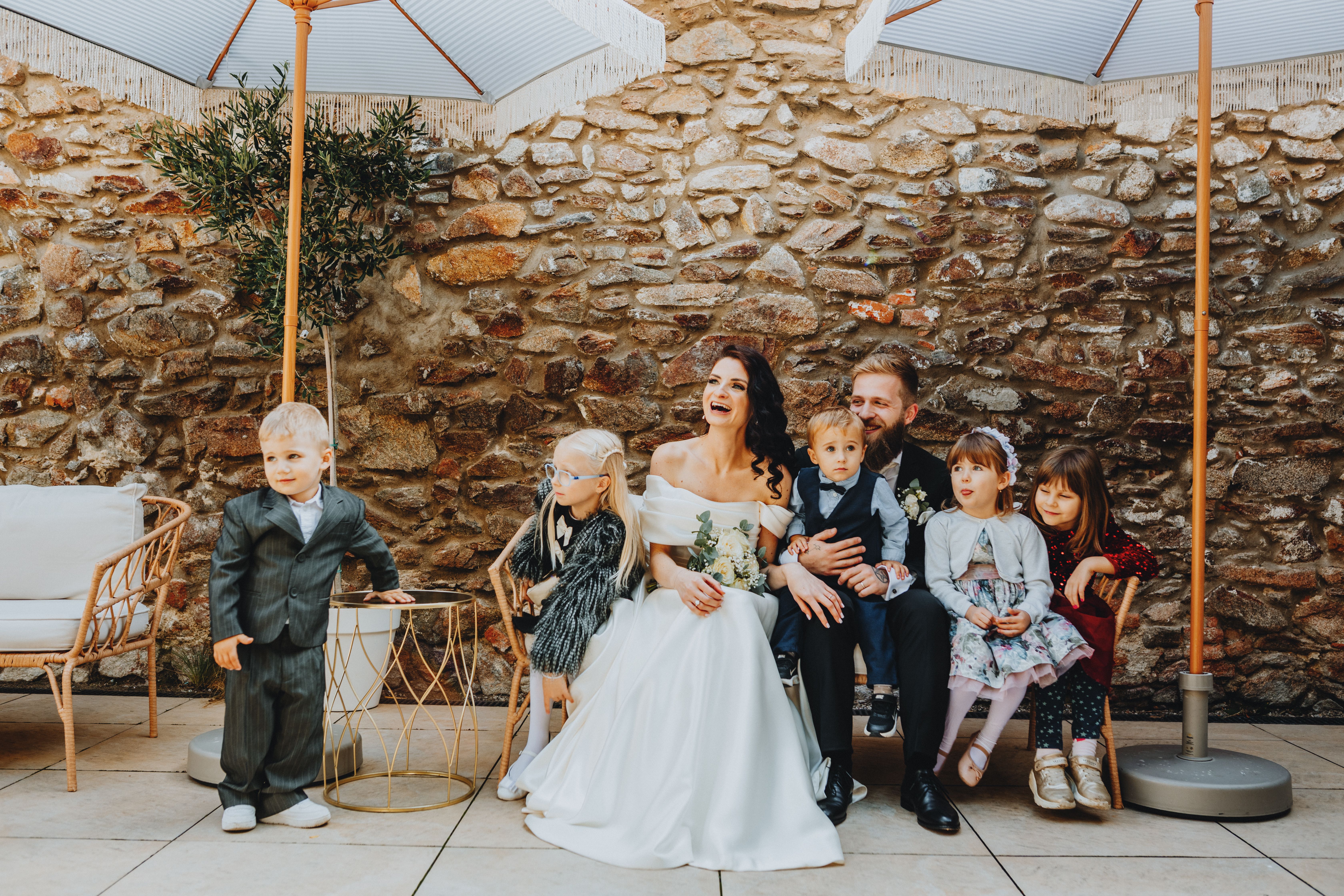 Happy family captured at a wedding against a rustic stone wall backdrop.