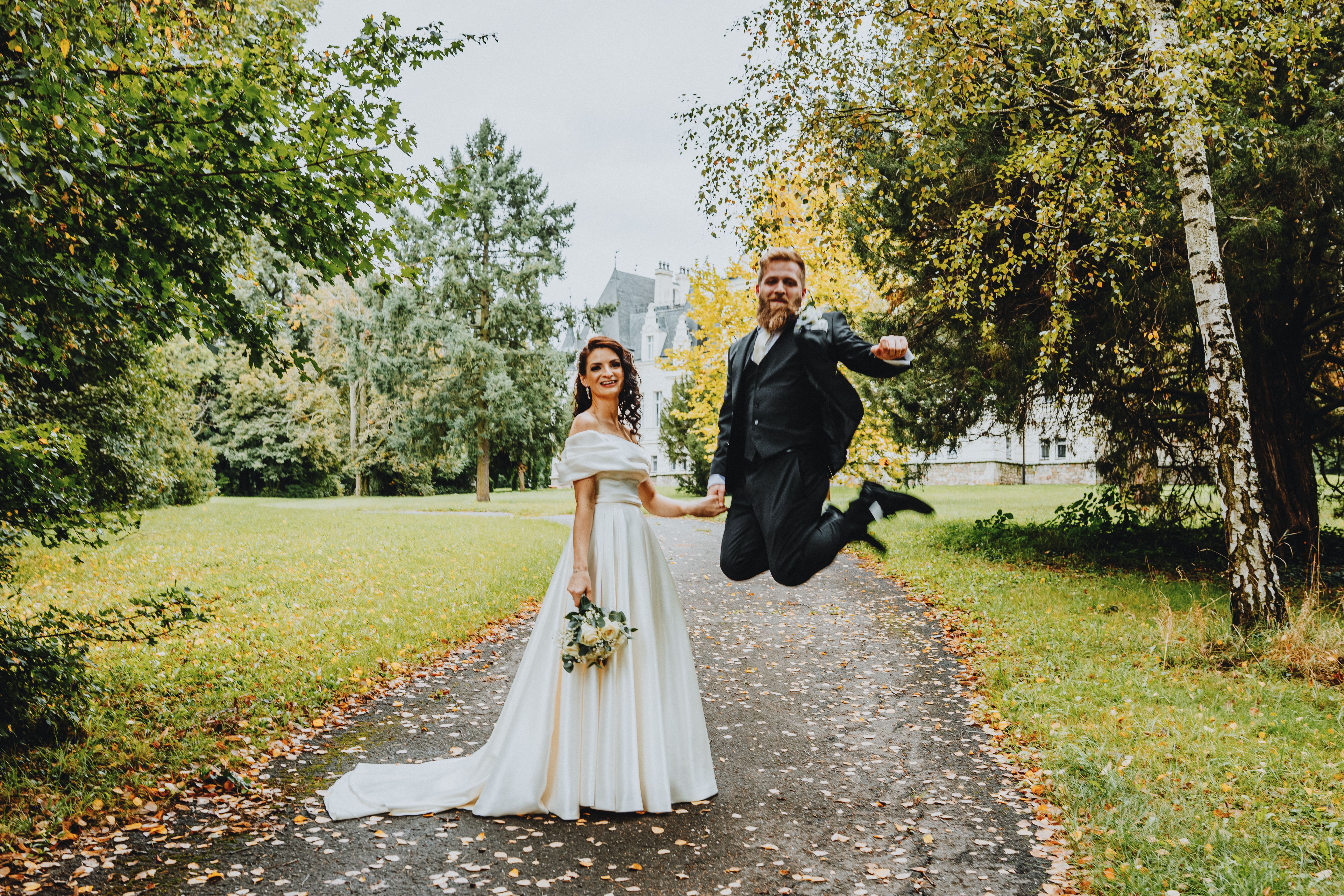 Bride and groom celebrating their wedding day with a joyful jump in a scenic autumn park.