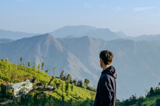 A young man in a hoodie surveys the scenic mountains of India in a morning vista.