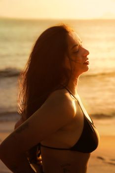 Woman in bikini enjoying the warm sunset on a tropical beach, feeling relaxed and free.