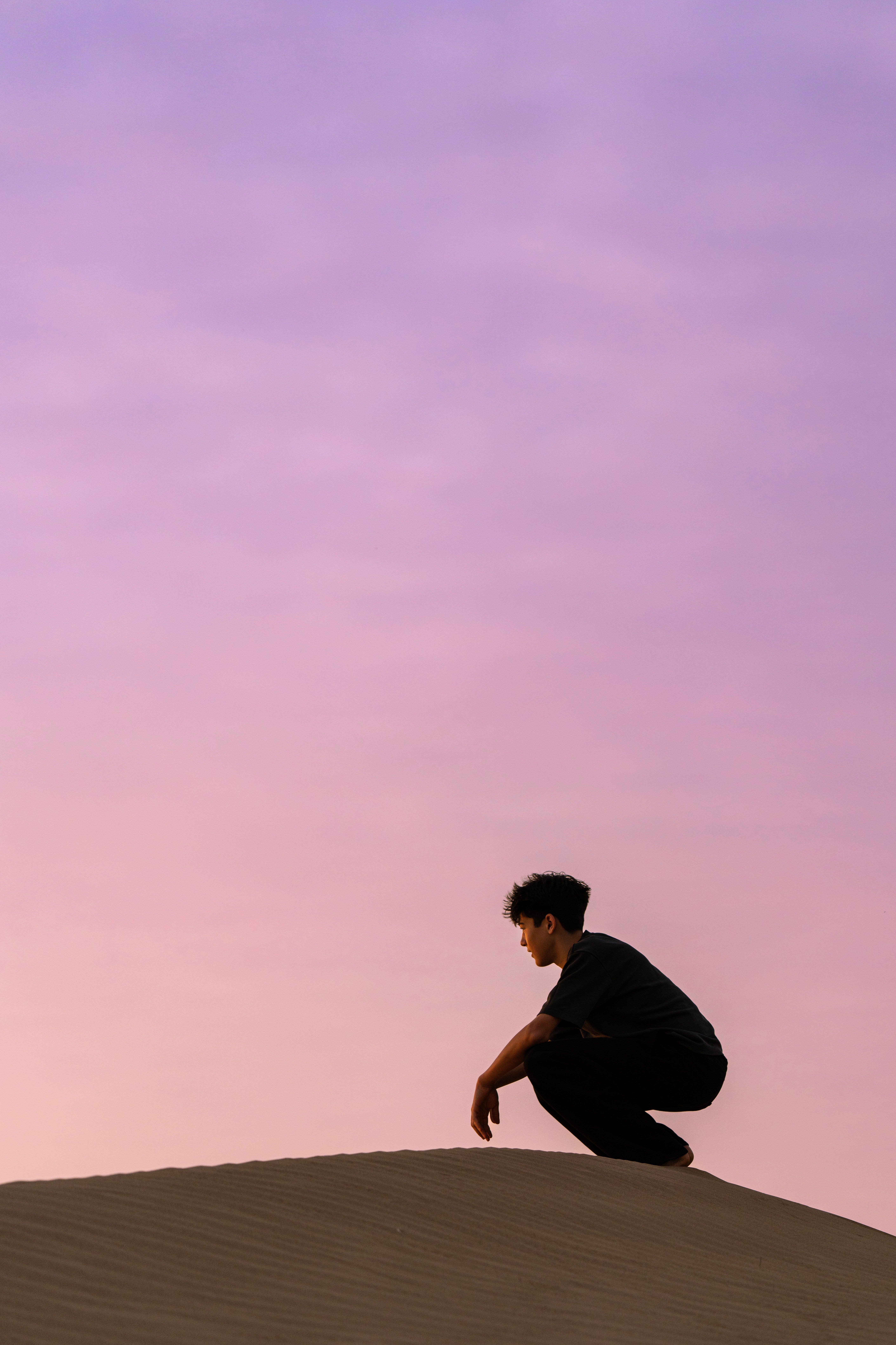 A person crouching on sand dunes with a vibrant sunrise sky in India, capturing a moment of introspection.
