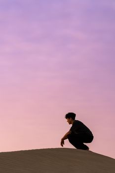 A person crouching on sand dunes with a vibrant sunrise sky in India, capturing a moment of introspection.