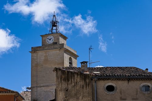 Free A clock tower in a historic French village against a vibrant blue sky with white clouds. Stock Photo