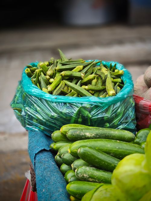 Free Close-up of fresh okra and cucumbers displayed at a market stall in transparent bags. Stock Photo