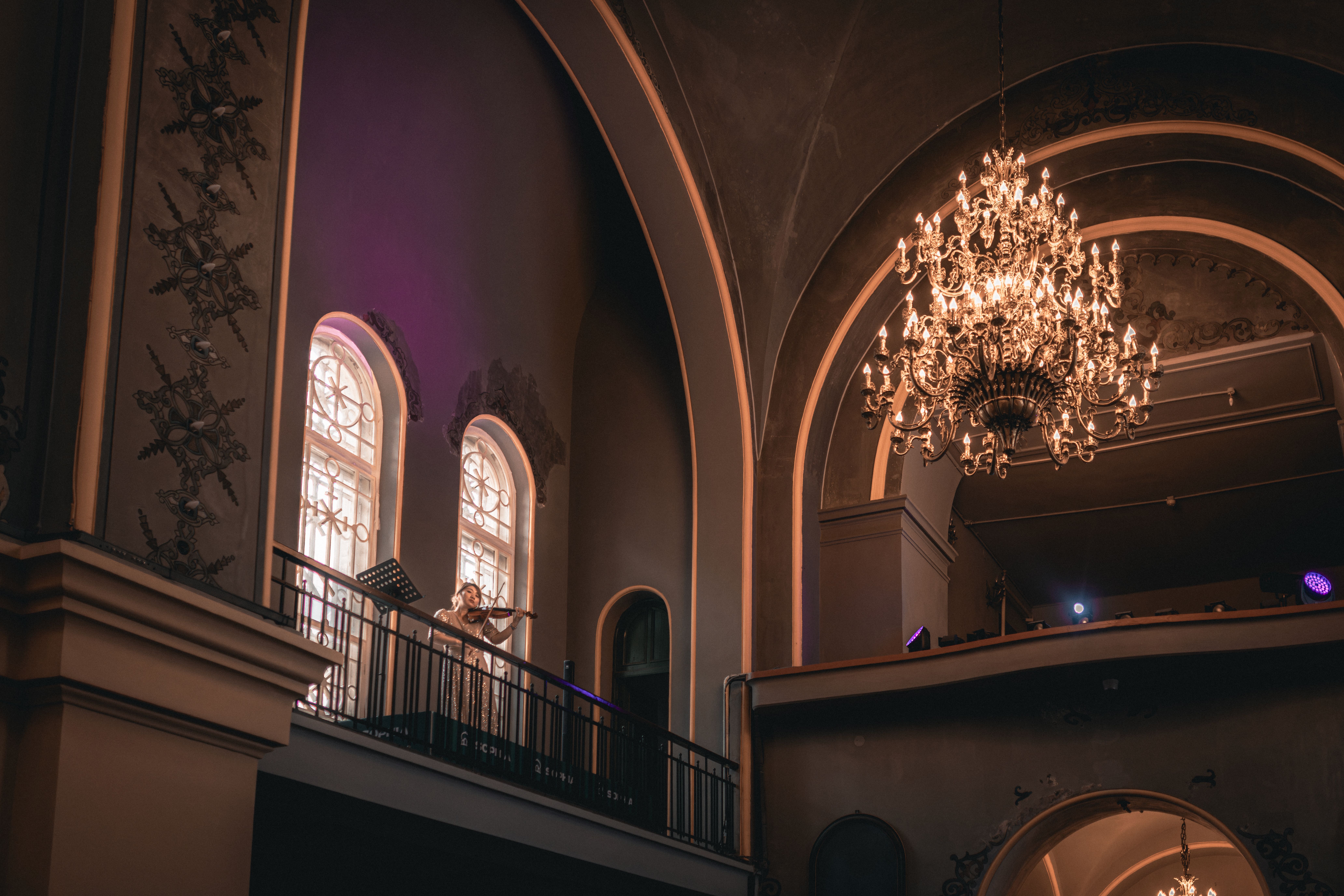 A violinist performs in a grand hall under a stunning chandelier.