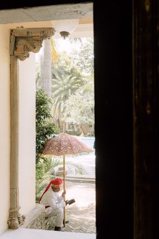 Man in traditional attire holding an ornate umbrella outside elegant building.