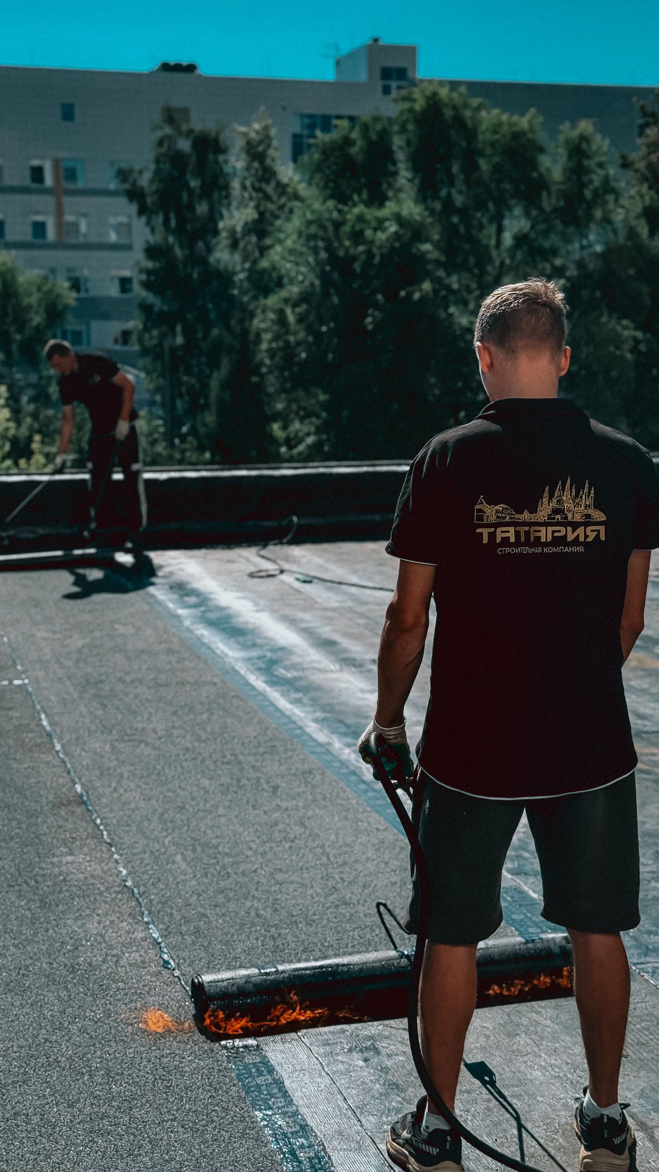 Two roofers applying a sealing coat to a flat roof in daylight