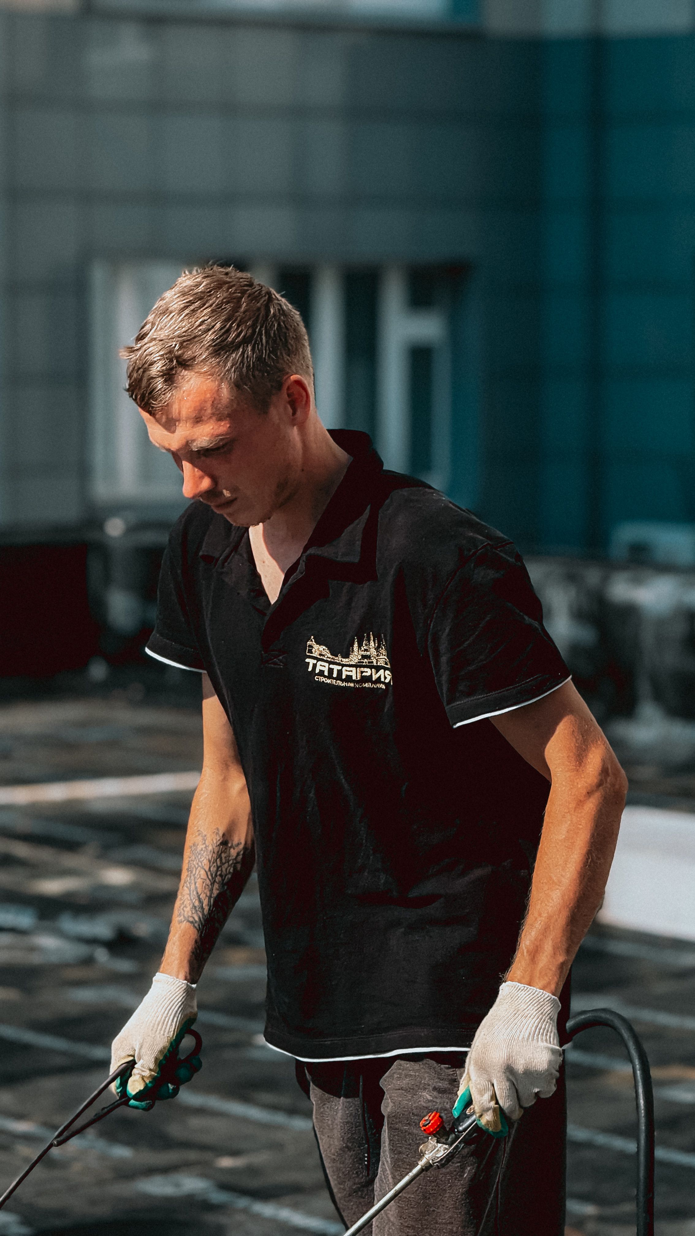 A man in work attire managing tools on a rooftop under the sun.