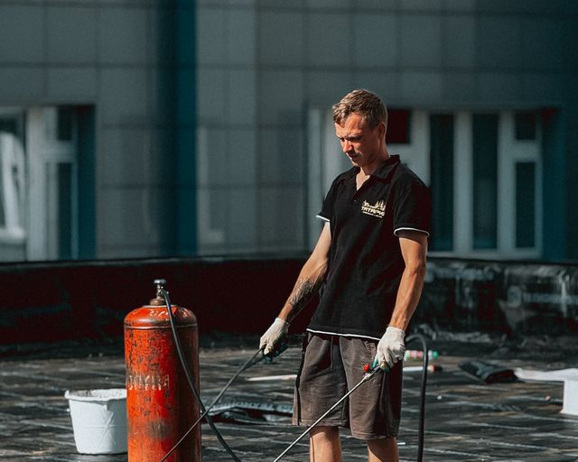 Modified bitumen install Roofer applying waterproof membrane on a rooftop with a gas cylinder nearby