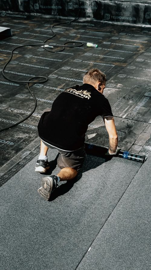 Free A construction worker installs asphalt roofing material under the sun, demonstrating professional craftsmanship. Stock Photo