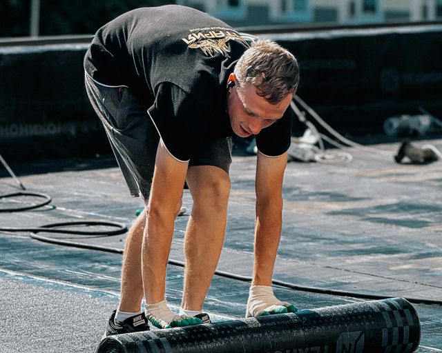 Waterproof membrane installation Worker placing a waterproof membrane on a flat roof under clear skies
