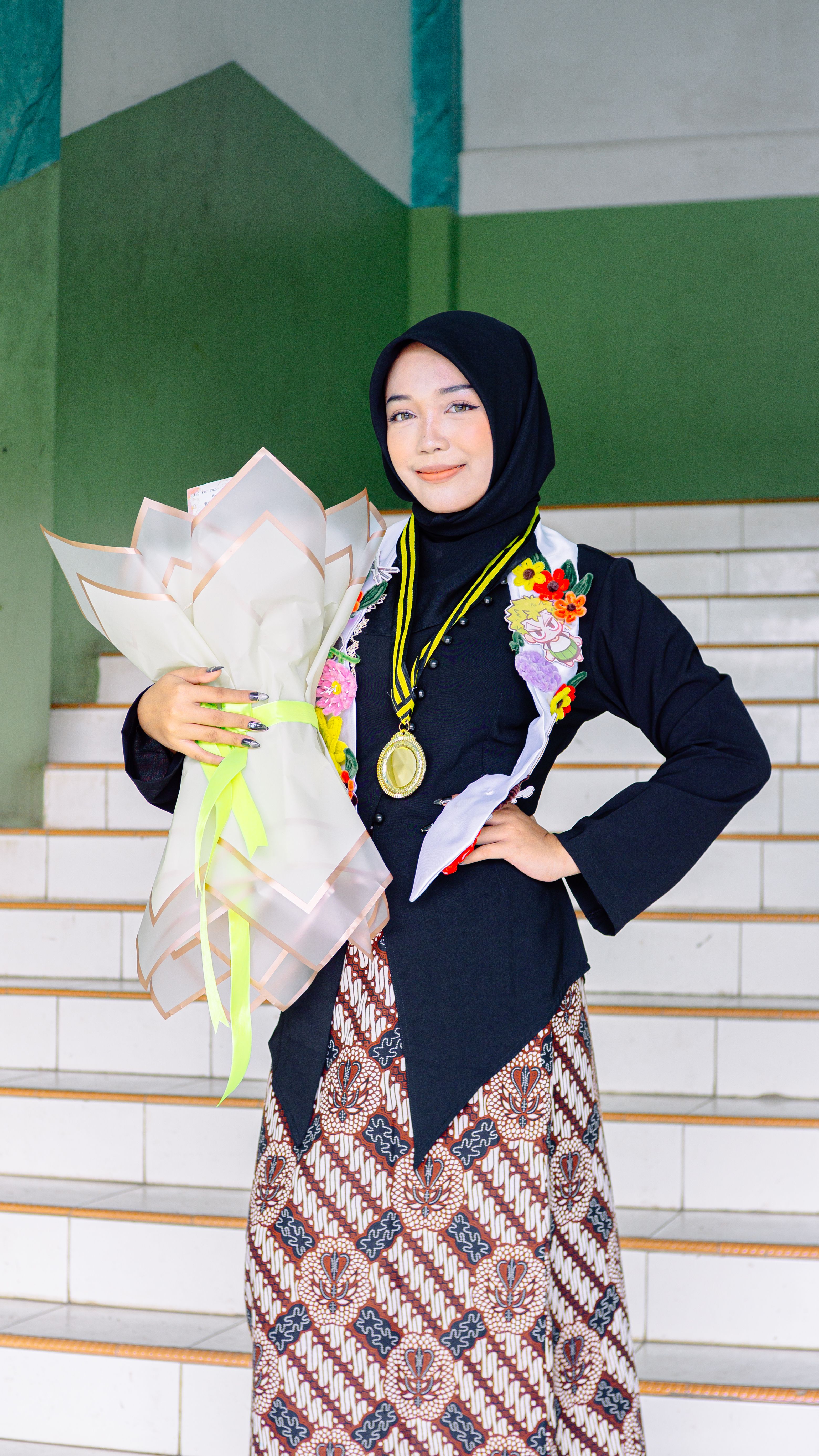 A young woman in traditional attire celebrating her graduation with flowers and a medal.