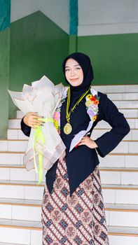 A young woman in traditional attire celebrating her graduation with flowers and a medal. - Fotografer Sidoarjo