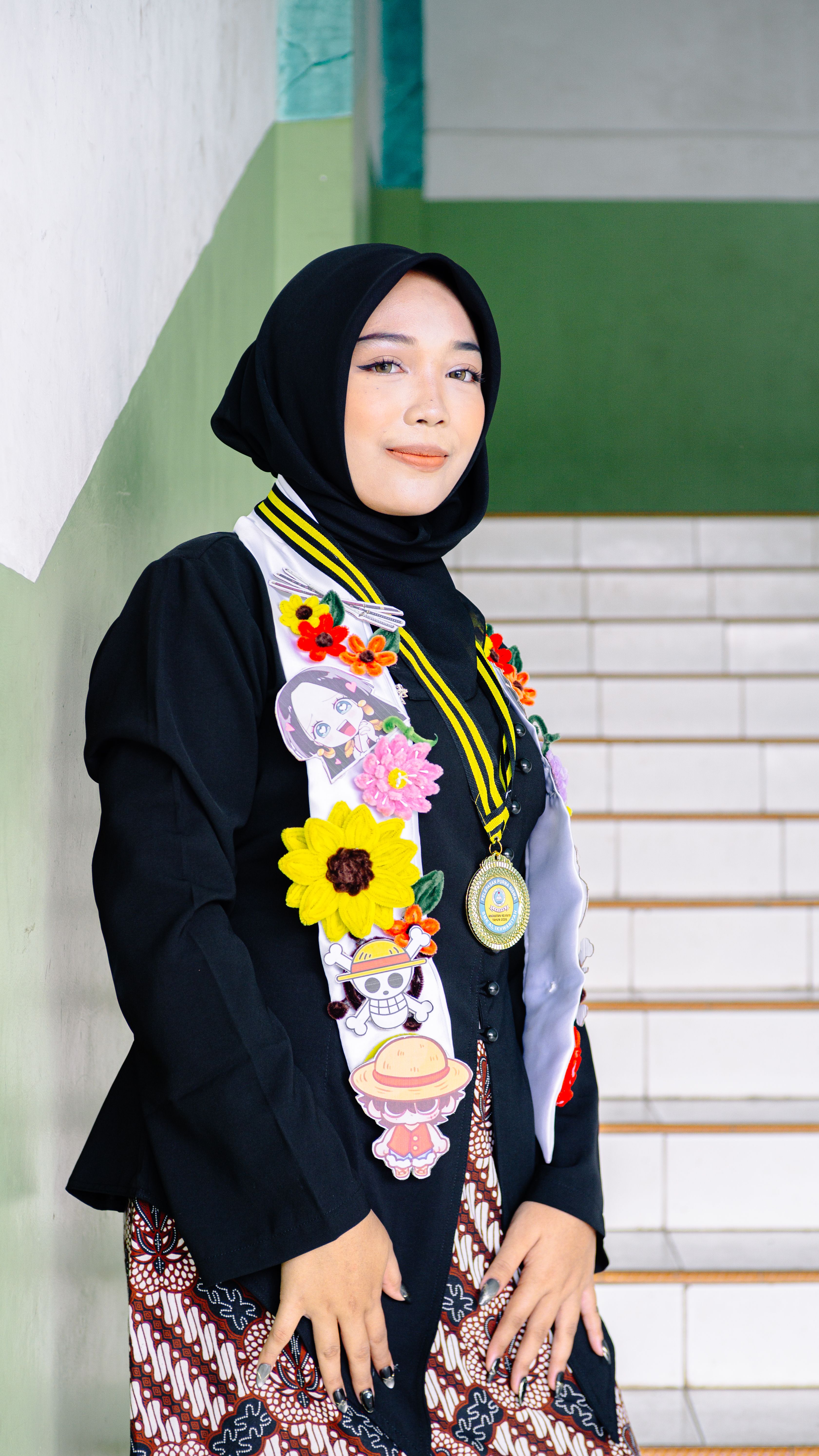 Young woman in hijab celebrating graduation with decorated sash on stairs.