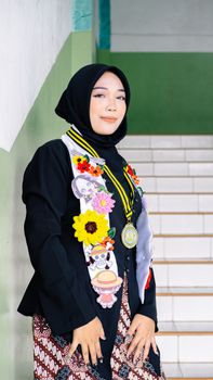 Young woman in hijab celebrating graduation with decorated sash on stairs. - Fotografer Sidoarjo