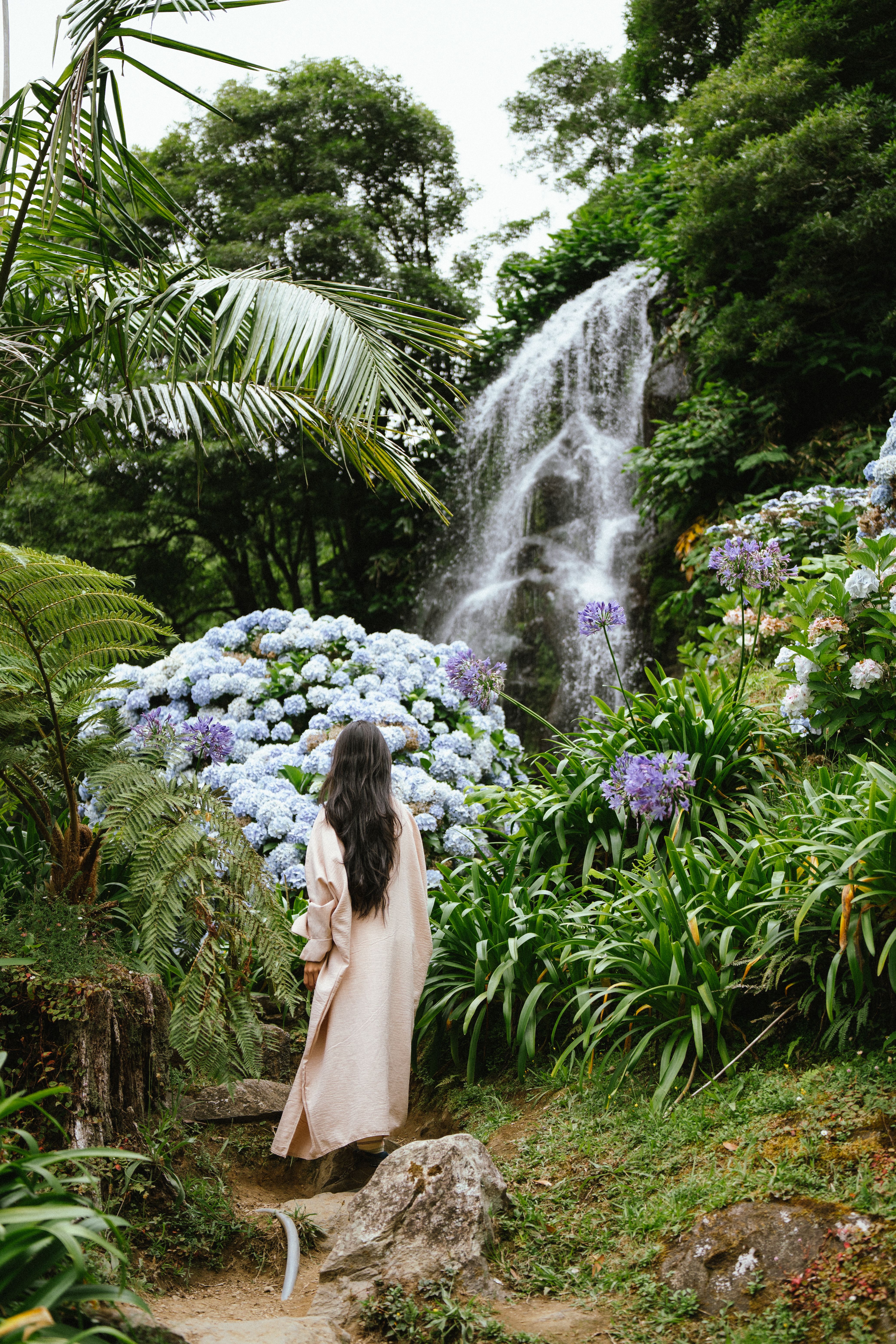 Woman in tranquil garden with hydrangeas and waterfall in Açores, Portugal.