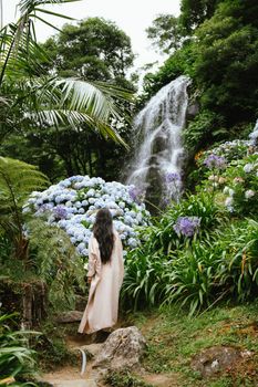 Woman in tranquil garden with hydrangeas and waterfall in Açores, Portugal.