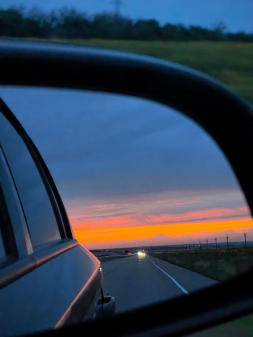 Free Colorful sunset view captured through a car side mirror during a highway drive. Stock Photo