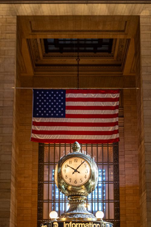 Free Grand Central Terminal clock under American flag, New York City iconic landmark. Stock Photo