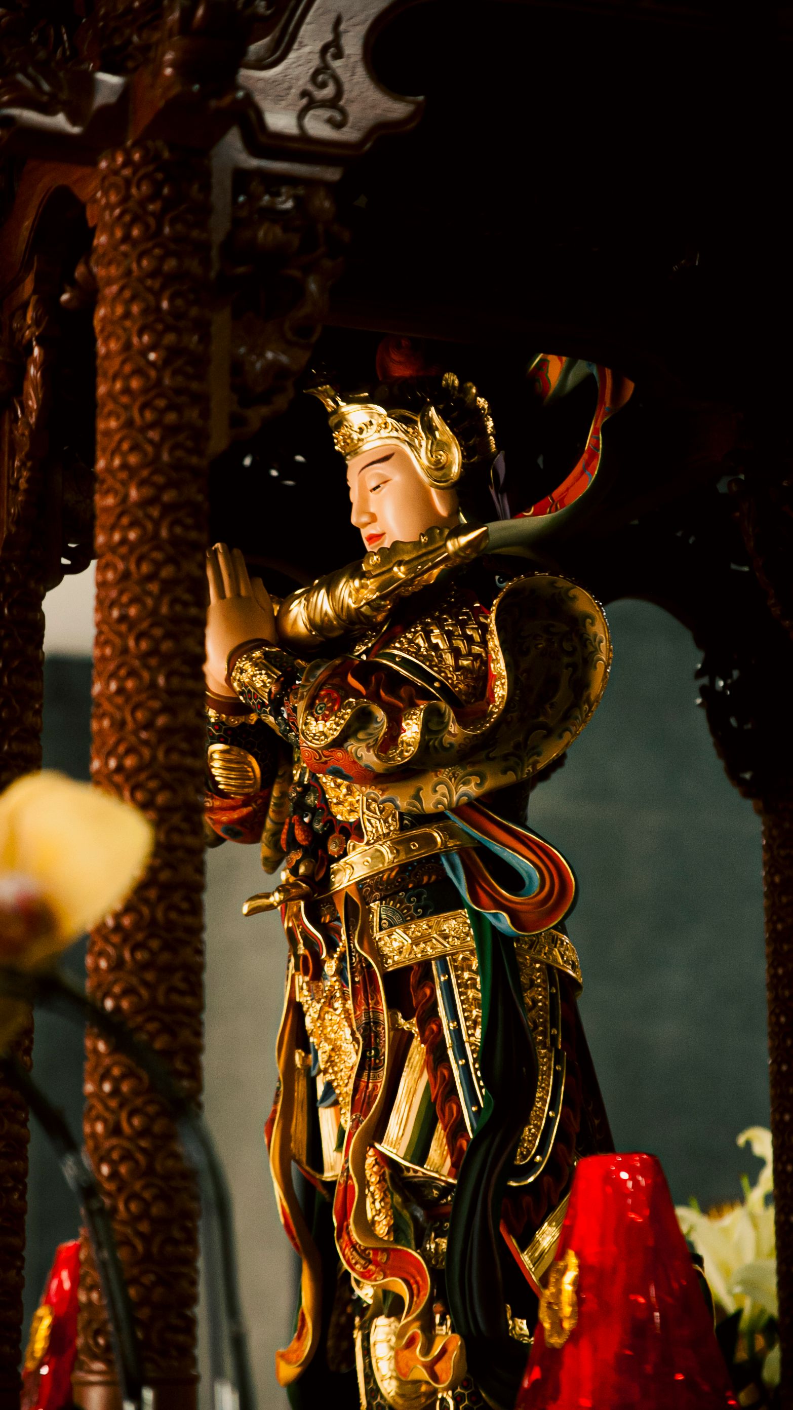 A detailed Asian warrior statue adorned with gold in a temple setting.