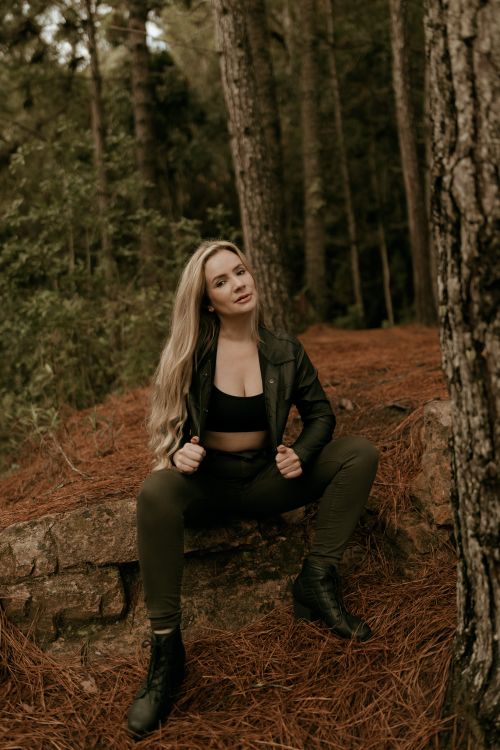 Free Stylish woman in forest wearing leather jacket and boots, striking a confident pose Stock Photo