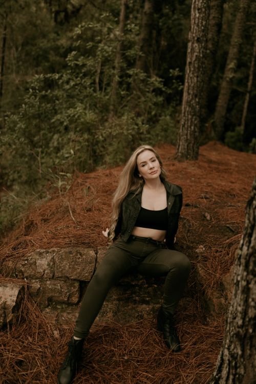 Free A young woman sitting on a forest floor surrounded by trees, embracing nature. Stock Photo