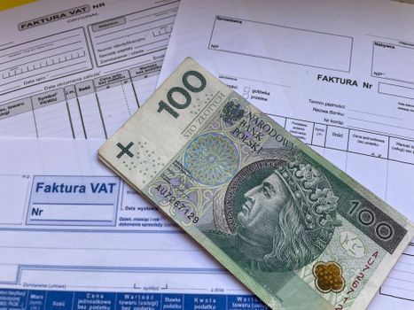A 100 Polish Zloty note placed on top of business VAT invoices, symbolizing finance and economics.