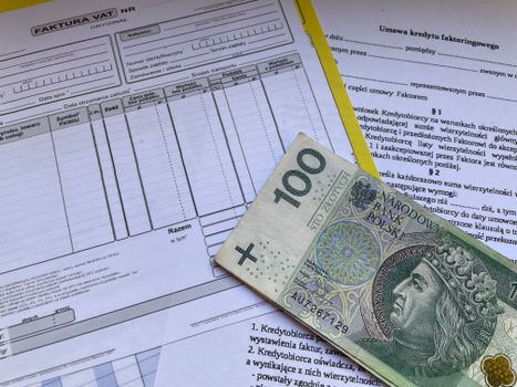 100 Polish zloty bill on top of financial documents and invoices on desk.