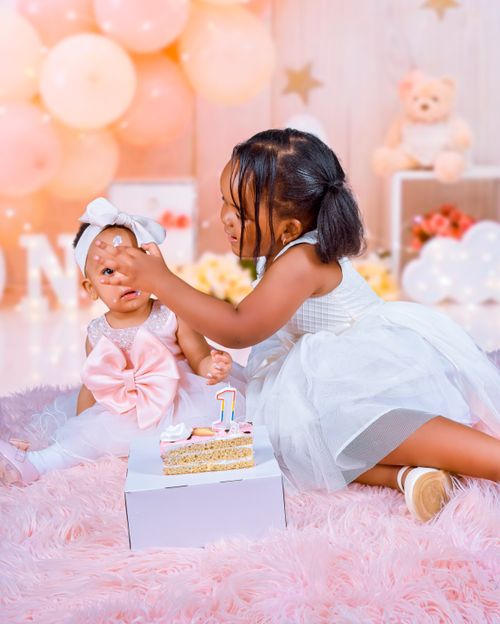 Free Two young siblings in a birthday setting sharing cake with pastel balloons and decorations. Stock Photo
