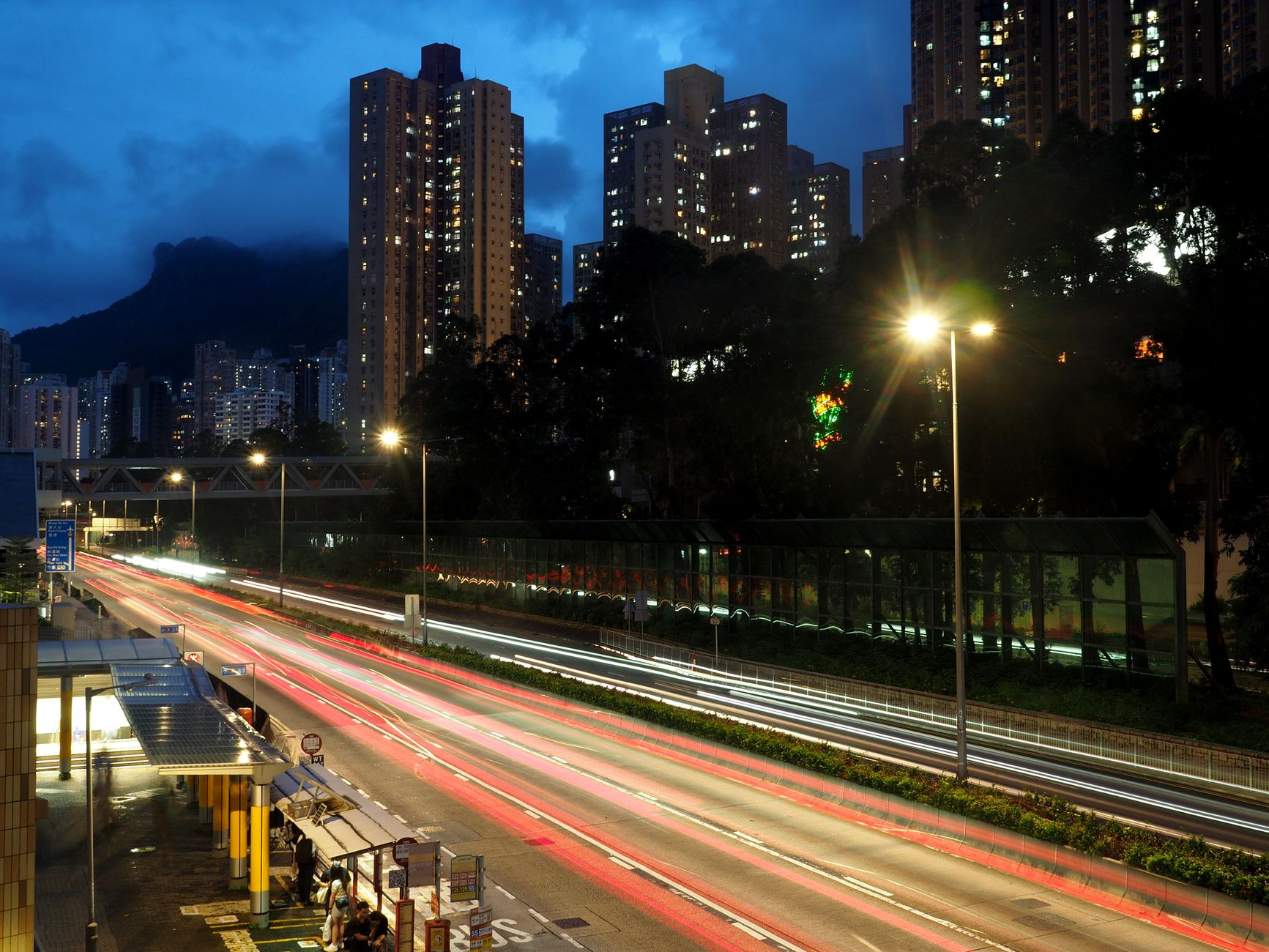 Night view of bustling Hong Kong streets with light trails and towering high-rise buildings.
