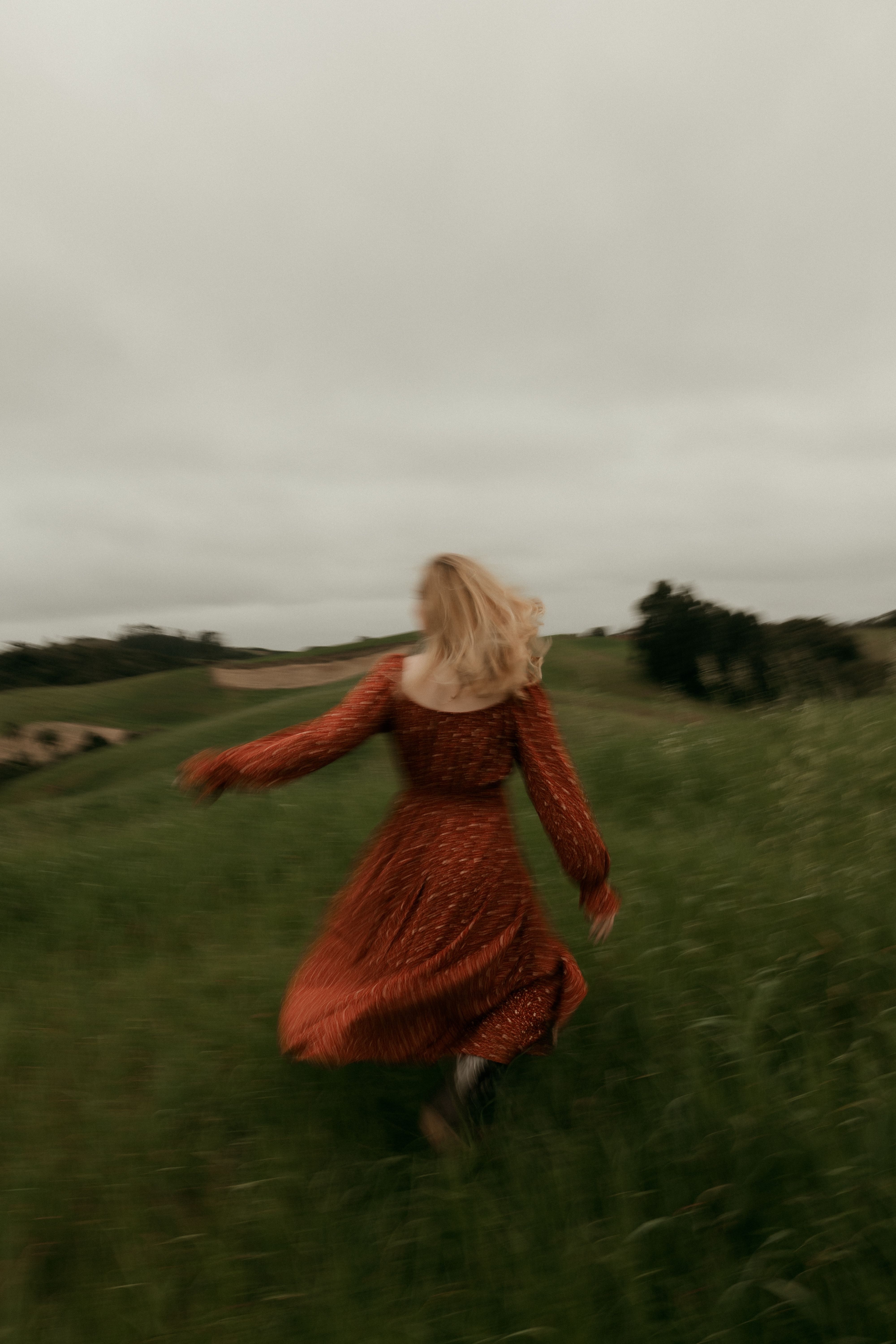 A woman in a flowing red dress runs freely through a lush green field.