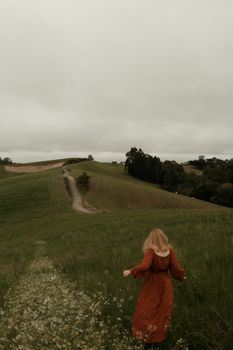 Woman in red dress exploring lush green hills under cloudy skies, perfect for travel and nature themes.