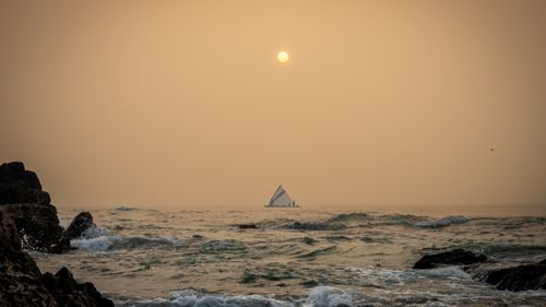 Free A serene view of a sailboat at sunset over the ocean near Visakhapatnam's rocky coast. Stock Photo