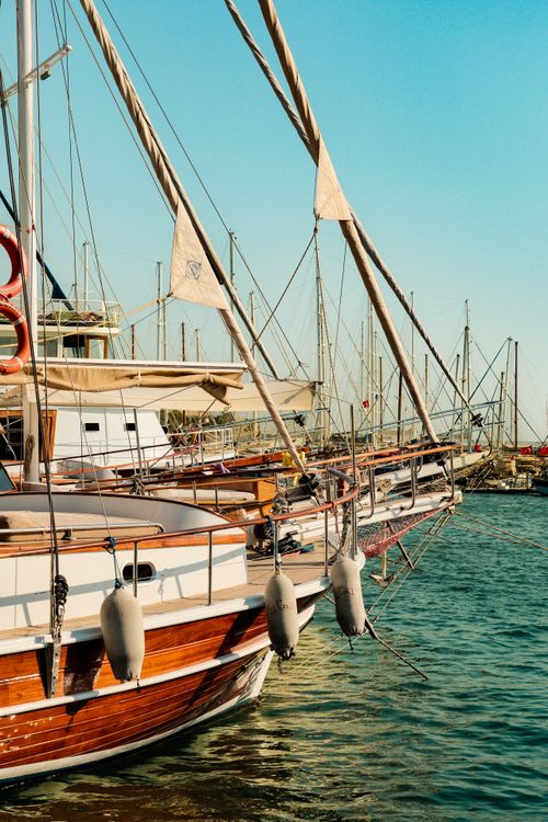 Free Rustic sailboats lined up in a serene marina with clear blue skies, perfect for travel enthusiasts. Stock Photo