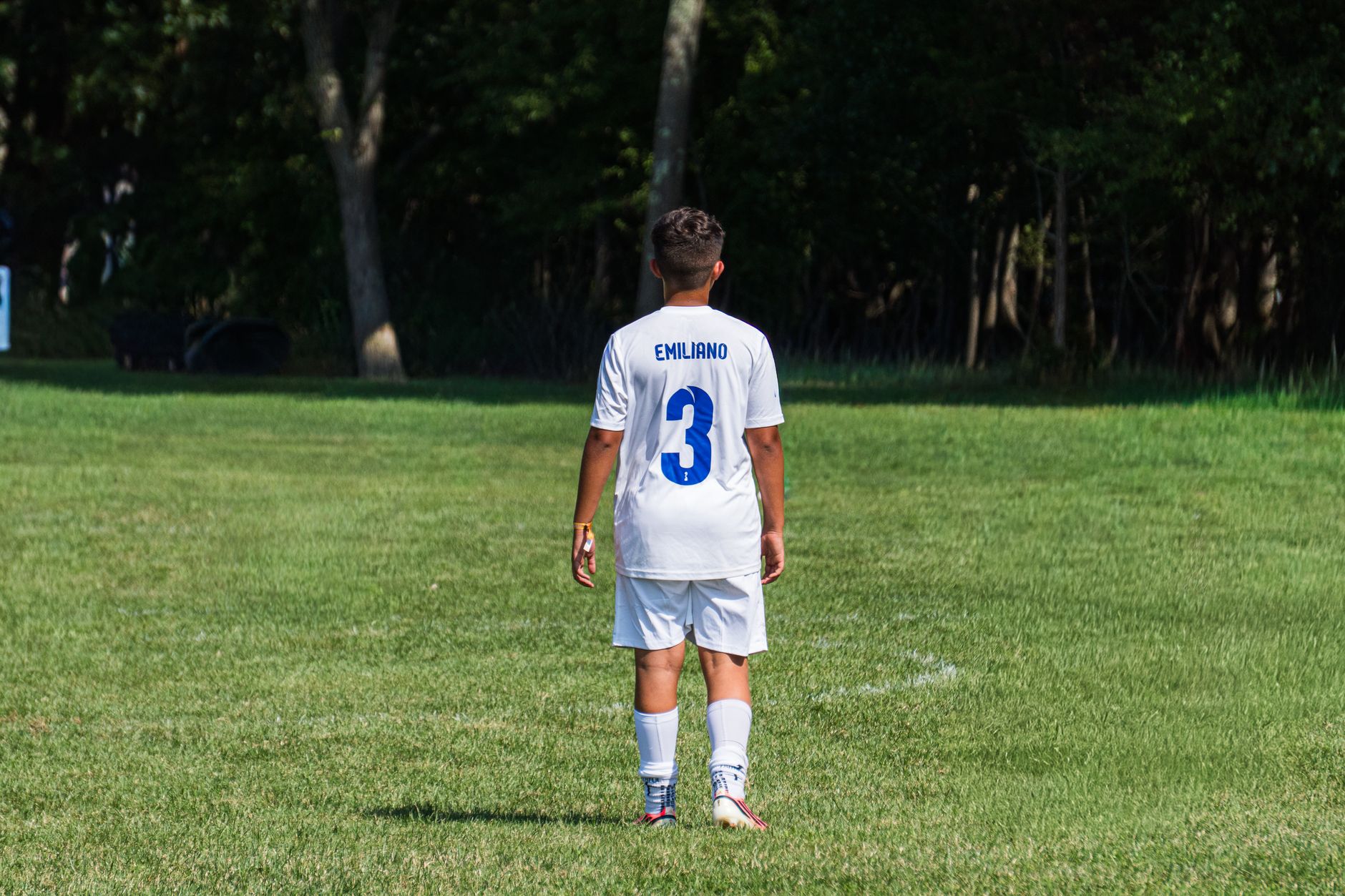 A young soccer player standing on a grassy field during a daytime match.