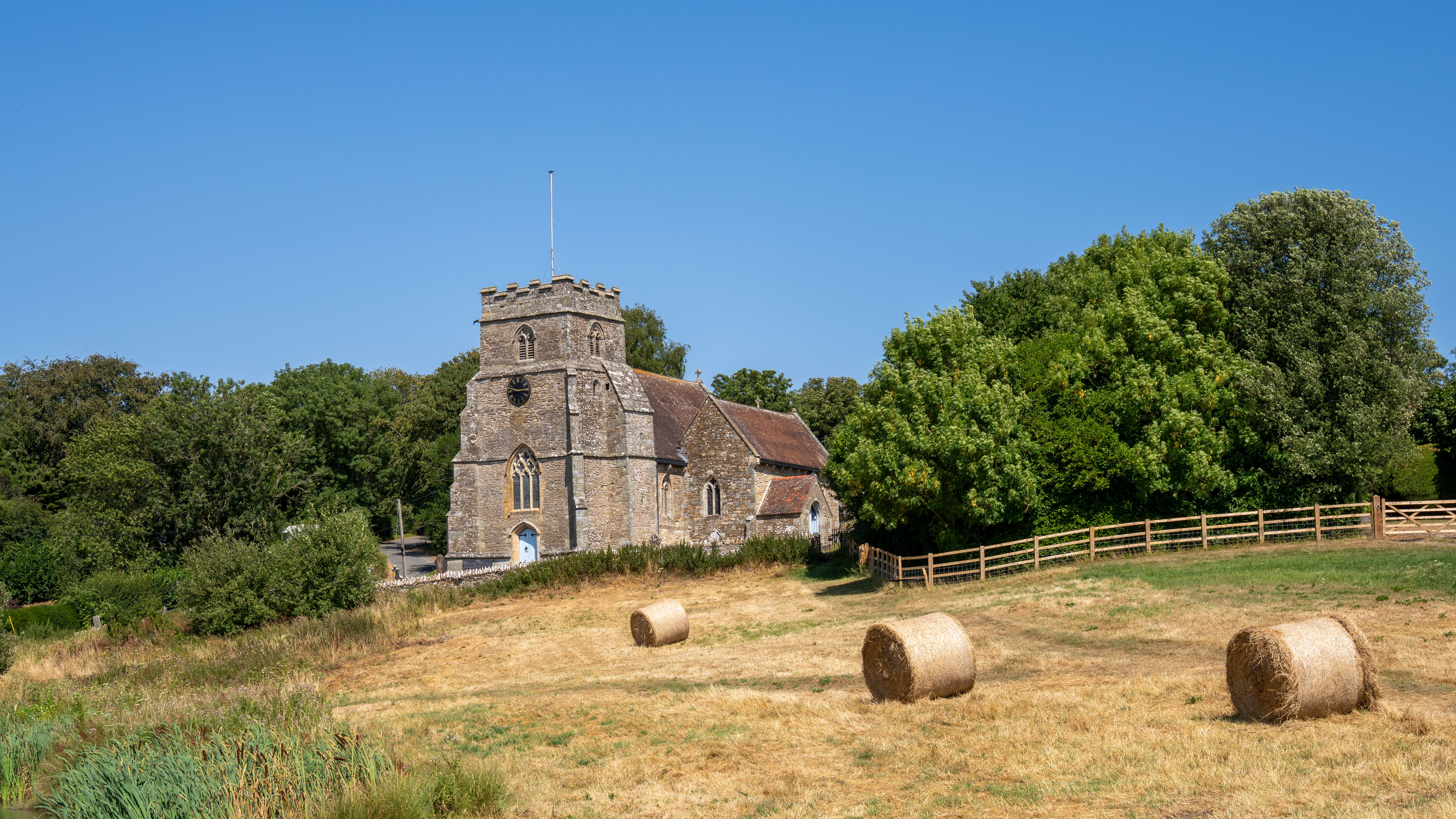 Charming stone church in Kington Magna, England, surrounded by hay bales and lush trees.