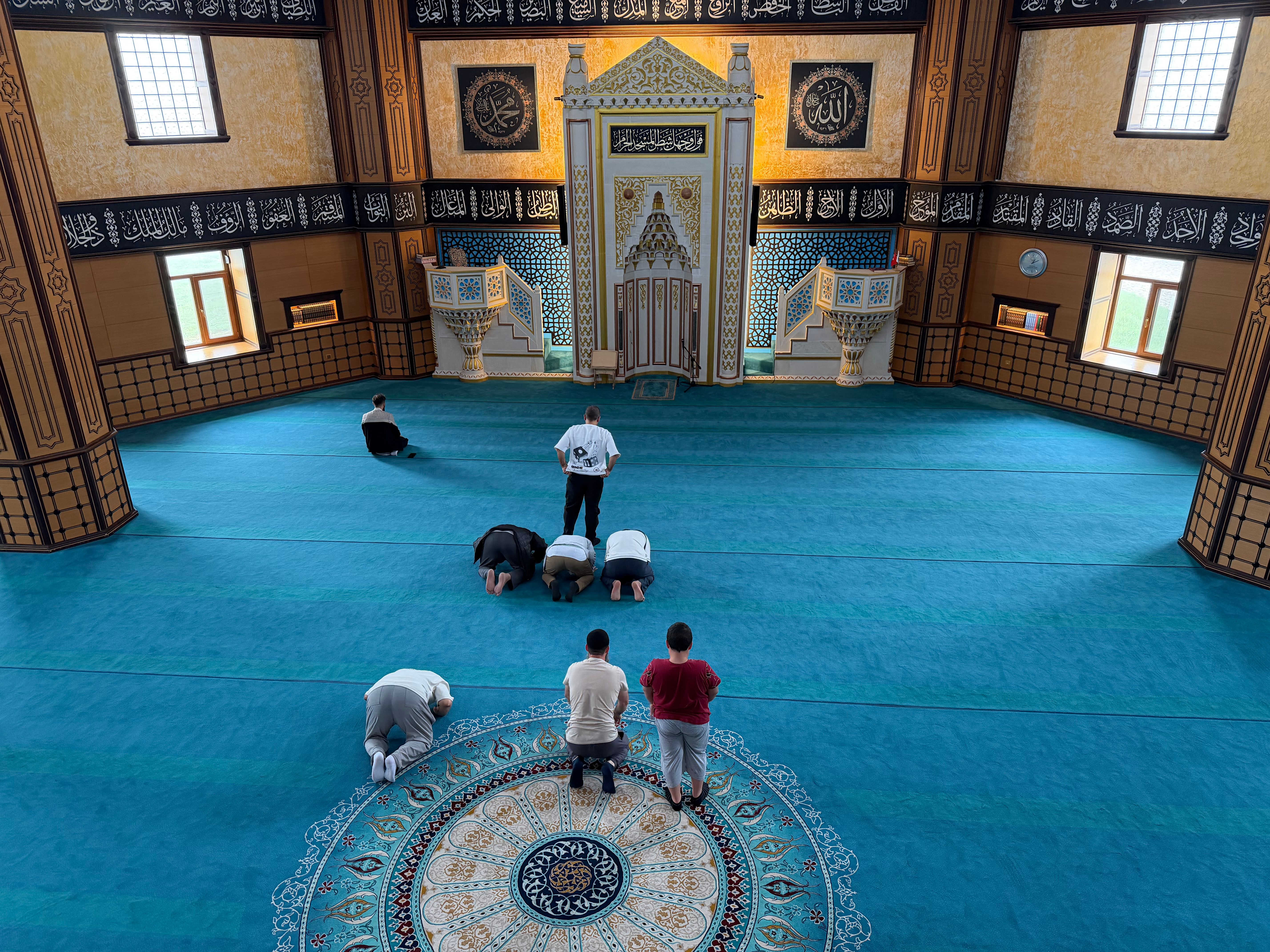 Men praying inside a beautifully decorated mosque, showcasing intricate Islamic architecture.